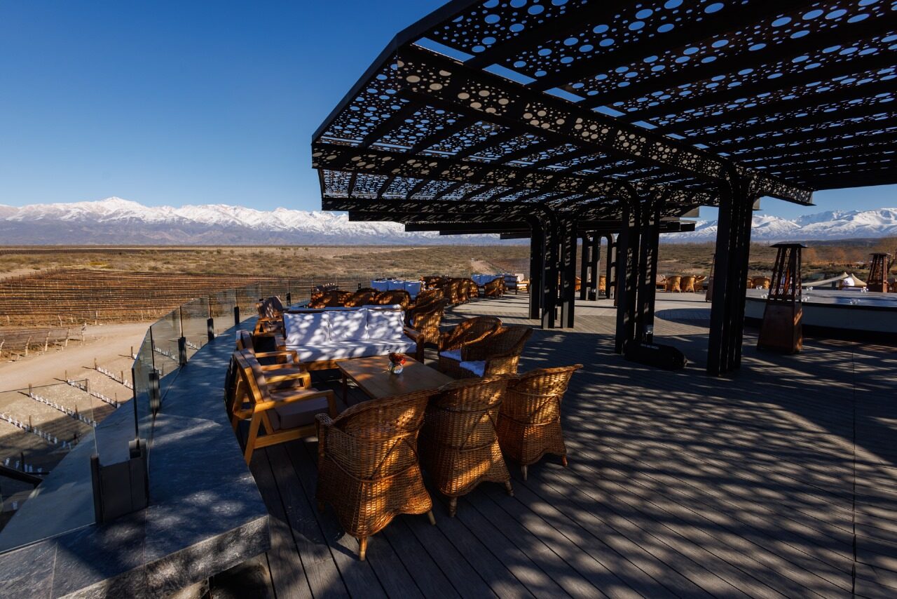 Mesa comprida posta sob pérgola de ferro no terraço de uma bodega em Gualtallary, com os Andes nevados ao fundo