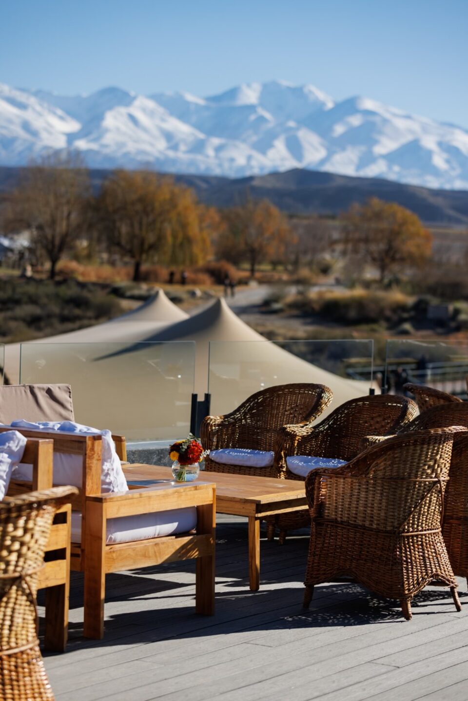 Poltronas de vime e mesa de madeira no terraço da bodega, com tenda beduína e os Andes nevados ao fundo